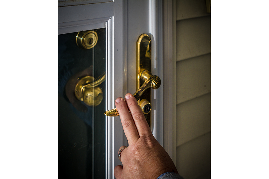A woman depresses the lever-handle of a screen door using only two fingers.